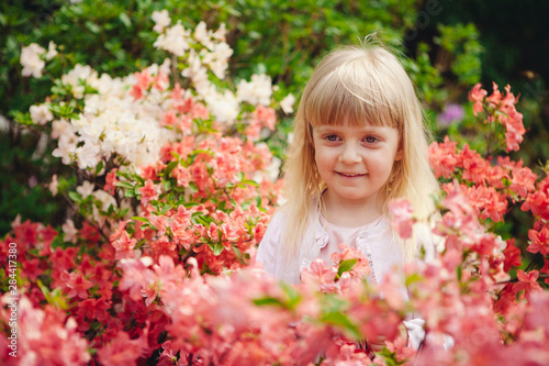 Little girl in park with azalea flowers, beautiful child on nature