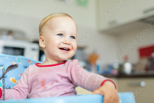 Adorable cute caucasian blond toddler boy eating tasty vegetable soup in chair at kithcen indoor. Mother feeding baby healthy food with spoon. Natural children nutriotion and diet