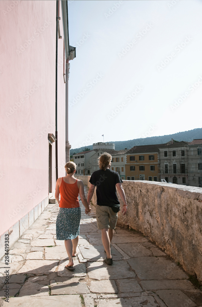 Cres, Coatia - Rear view of a young couple strolling along a terrace.