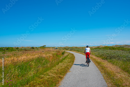 Bicycling on a small bike road thorugh an open, green landscape on a sunny day.