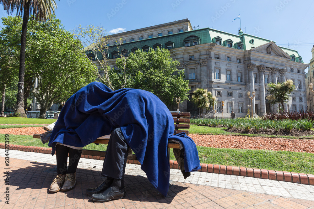 Argentina, Buenos Aires. People sitting on park bench under blanket.