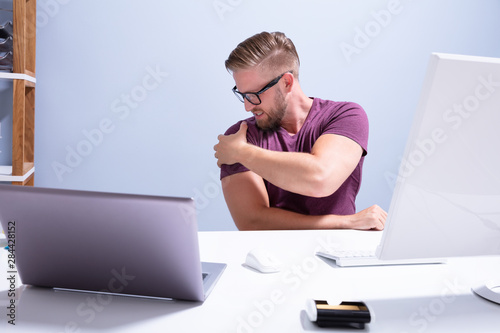 Man Sitting On Chair Suffering From Shoulder Pain