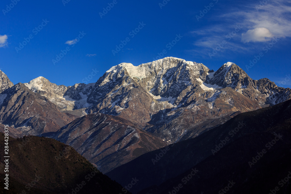 Snow Mountain, Cliffs, Jagged Steep Rock Face, extreme vertical drop, Blue Sky White Clouds in Background, Landscape Graphic Image.
