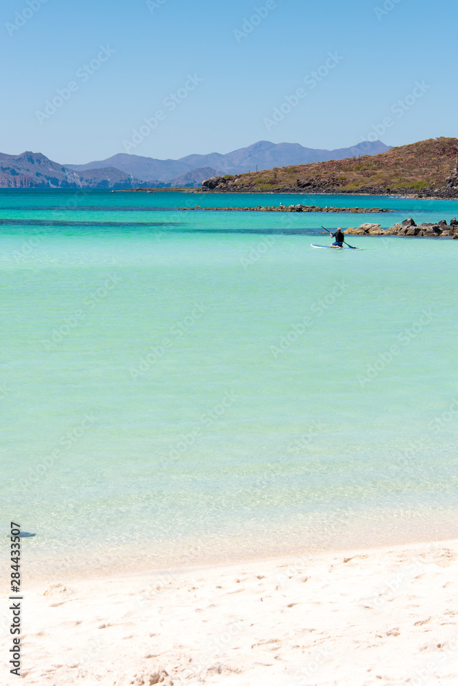 Mexico, Baja California Sur, Sea of Cortez. White sand beach and calm waters Isla Coronado. Paddleboarder kneels