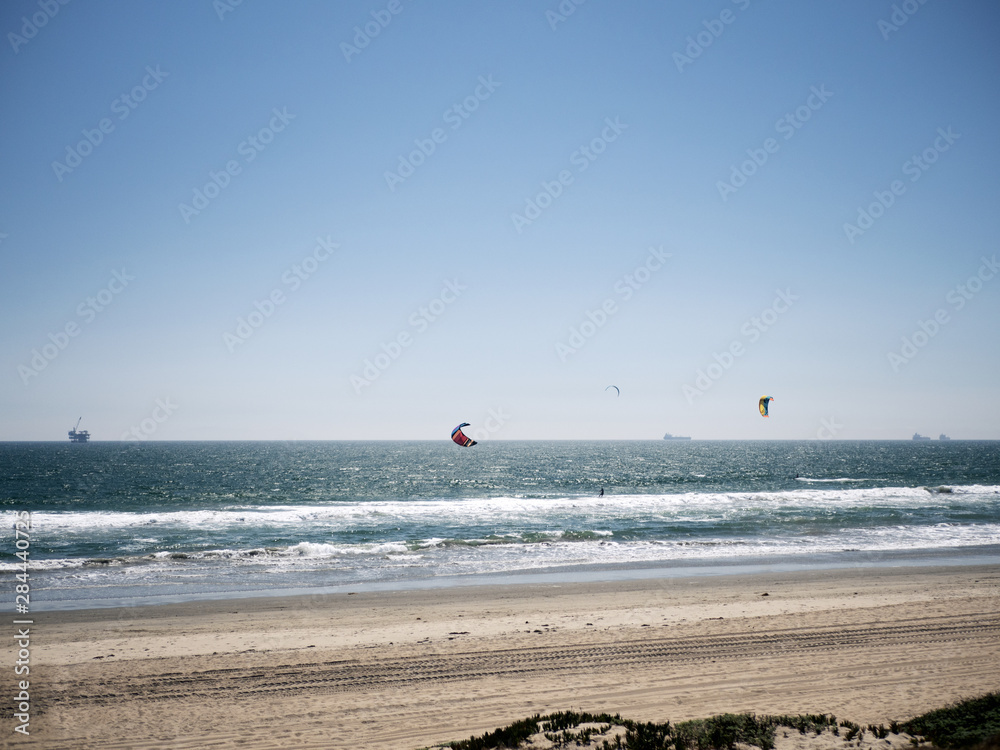 Three kite surfers and an oil rig at the beach.