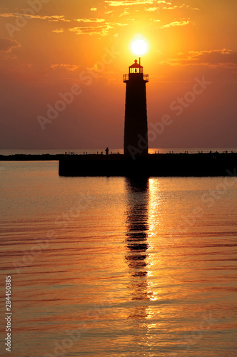 USA, Michigan, Muskegon. The setting sun silhouettes the lighthouse on Lake Michigan in Muskegon, Michigan.