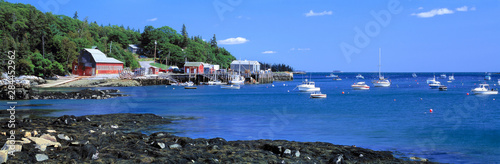 USA, Maine, Tenants Harbor. The bright blue waters of Tenants Harbor contrast the red shoreline buildings of Knox County, Maine.