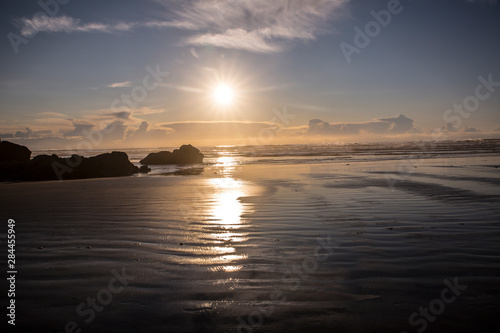 Cannon Beach, Oregon. Sunburst as the sun sets over the Pacific Ocean, tide pools, haystack rocks, and wet sand © Jolly Sienda/Danita Delimont
