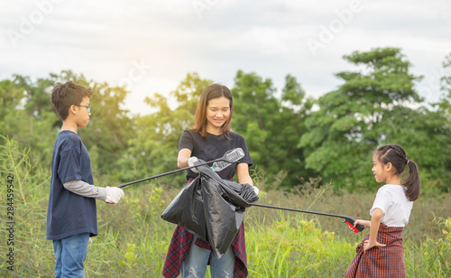 Selective focus of Mother and child collecting garbage on a meadow on evening day, Save environmental concept