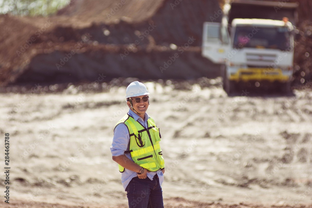 portrait mining worker or engineer in reflective vest and hardhat posing with hand inside pocket in front of white truck at coal and soil mining site portrait mining worker or engineer in reflective vest and hardhat posing with hand inside pocket in front of white truck at coal and soil mining site