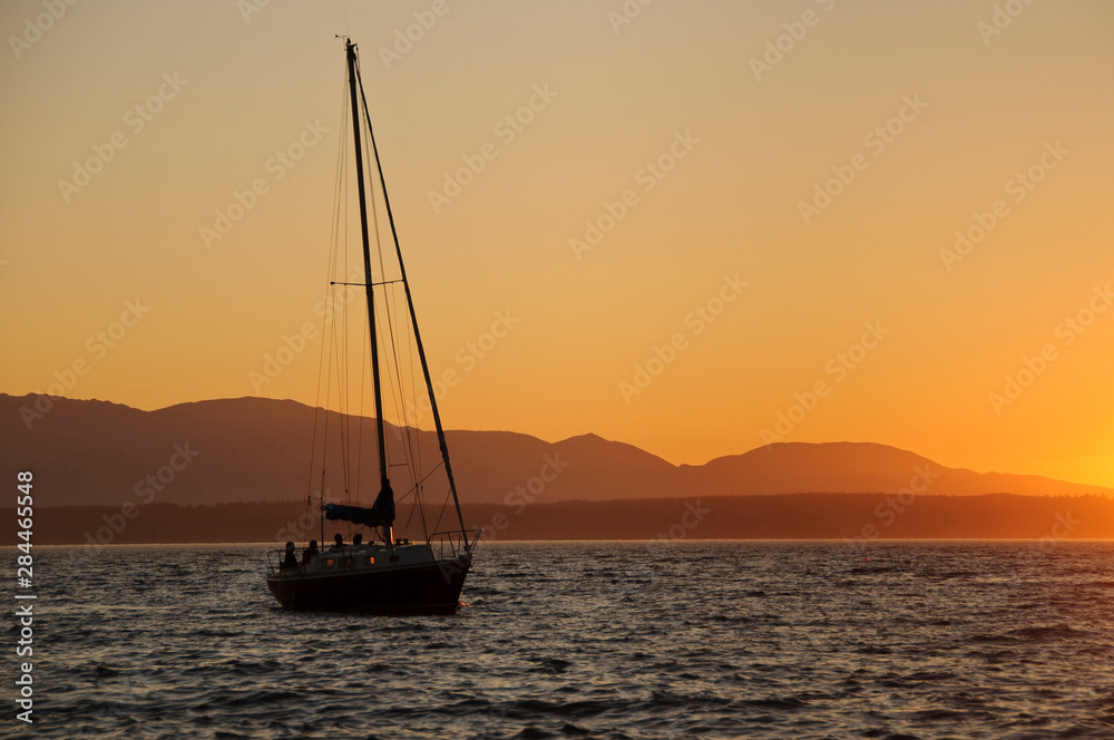 Sailboat at sunset on the Puget Sound. Olympic Mountains in background.
