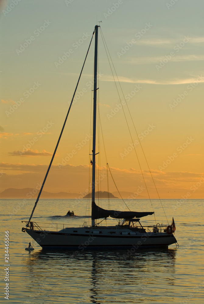 USA, WA, San Juan Islands. Departing sailboat in loaded dinghy silhouetted by setting sun.