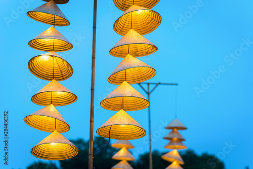 Illuminated stripe Vietnamese traditional conical hats hanging on wire for decoration, with blue sky at twilight photo