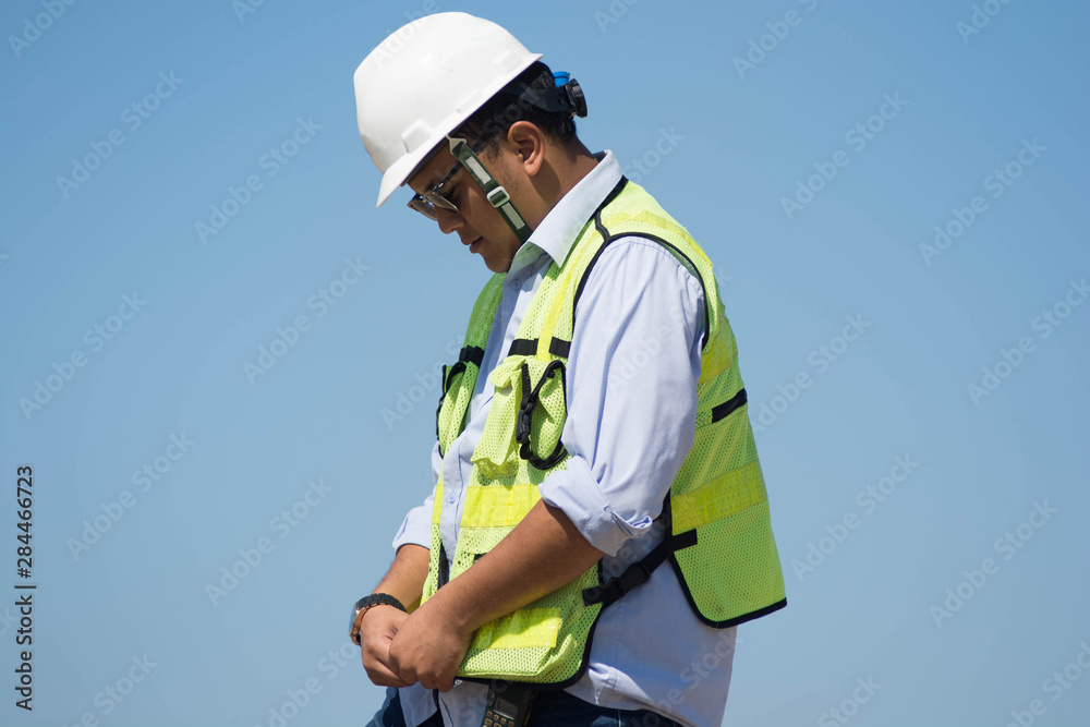 bottom rear view of male engineer walking and holding tablet computer on bright blue sky for planing a construction dress with protective vest, hard helmet bottom rear view of male engineer walking and holding tablet computer on bright blue sky for planing a construction dress with protective vest, hard helmet