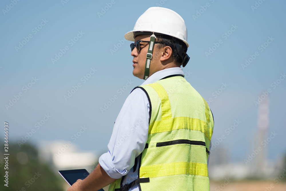 rear view of male engineer walking and pointing on bright blue sky for planing a construction dress with protective vest, hard helmet rear view of male engineer walking and pointing on bright blue sky for planing a construction dress with protective vest, hard helmet