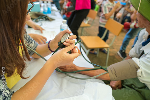 Volunteer nurse measuring blood pressure of poor Asian people outdoors closeup