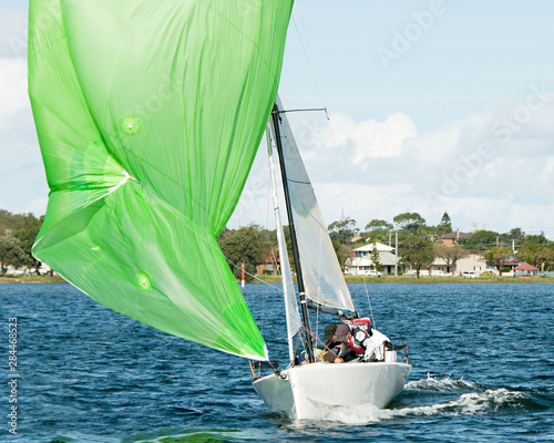 Kids sailing small sailboat head-on closeup with a fouled green spinnaker. photo