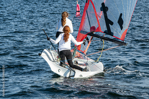 Two Girls Sailing small sailboat with long red hair viewed closeup from behind.