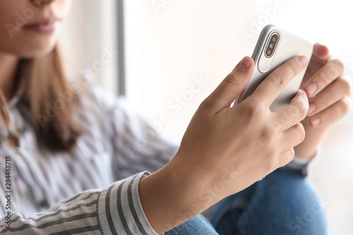 Young woman holding mobile phone on light background, closeup with space for text. Loneliness concept photo