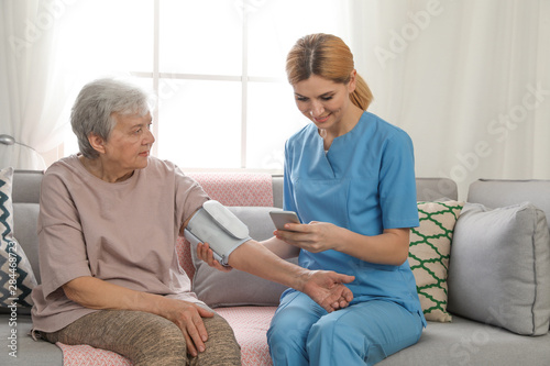 Nurse measuring blood pressure of elderly woman indoors. Assisting senior people