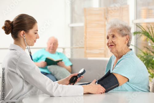 Nurse measuring blood pressure of elderly woman indoors. Assisting senior generation