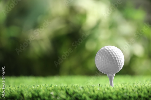 Golf ball with tee on artificial grass against blurred background, space for text