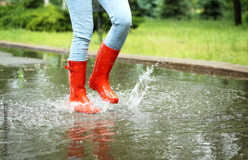 Woman with red rubber boots jumping in puddle, closeup. Rainy weather