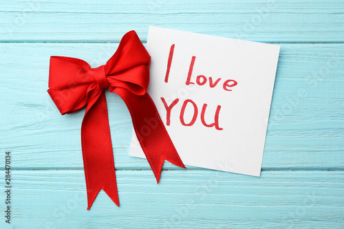 Red bow and note with words I LOVE YOU on blue wooden table