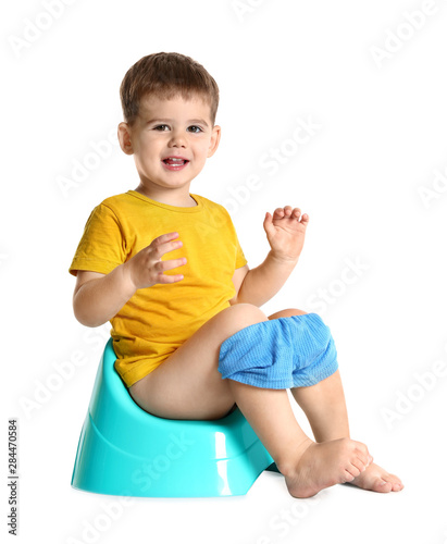 Portrait of little boy sitting on potty against white background photo