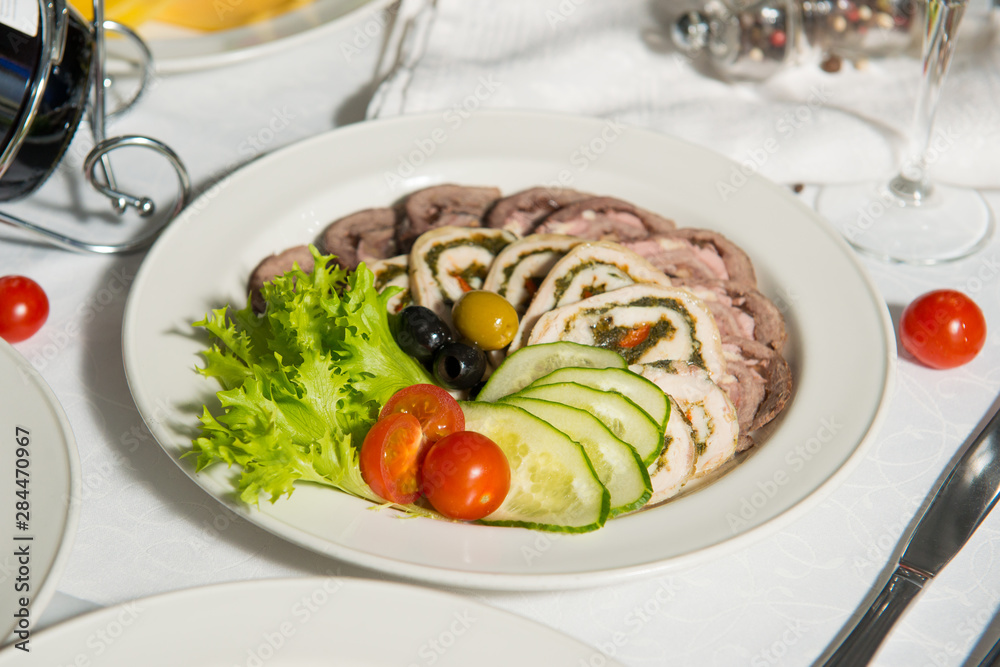 A restaurant dish of slicing meatloaf with vegetables on a table in a plate. Cold appetizer.