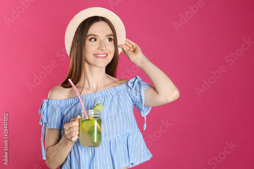 Beautiful young woman with Mason jar of natural detox lemonade on pink background. Space for text