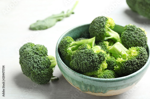 Bowl and fresh broccoli on light grey table, closeup