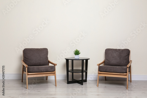 Room interior with modern armchairs and table near light wall