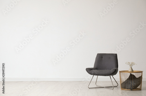 Stylish living room interior with comfortable chair and side table near white wall. Space for text