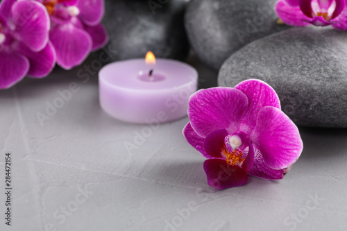 Spa stones  orchid flowers and candle on grey table  closeup