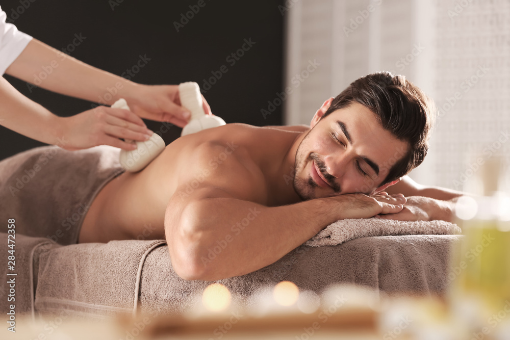 Handsome young man receiving herbal bag massage in spa salon
