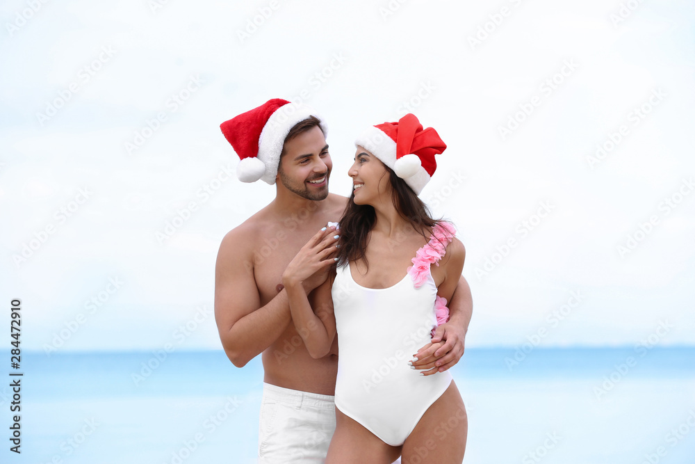 Obraz premium Happy young couple with Santa hats together on beach