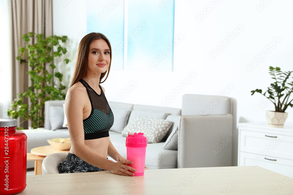 Young woman with bottle of protein shake at home. Space for text Young woman with bottle of protein shake at home. Space for text