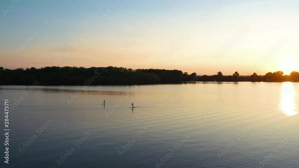 Silhouette of Couple Paddle Boarding on Lake Under Beautiful Sunset Sunlight, Drone Aerial Silhouette of Couple Paddle Boarding on Lake Under Beautiful Sunset Sunlight, Drone Aerial