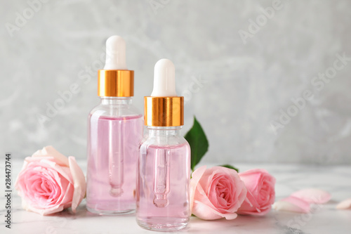Bottles of essential oil and roses on marble table