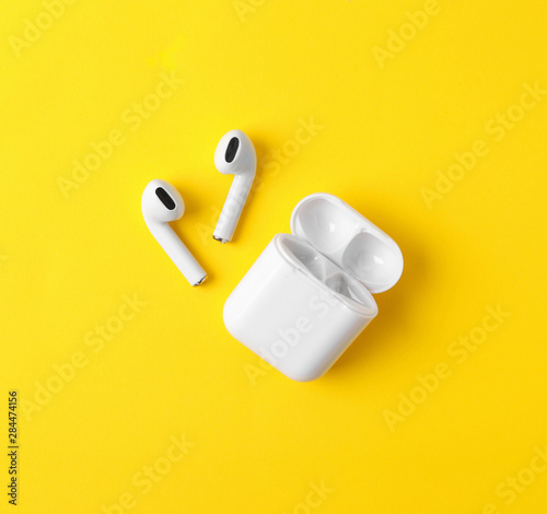 Modern wireless earphones and charging case on yellow background, flat lay