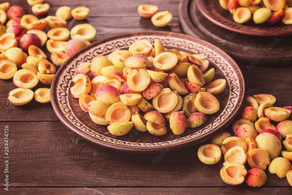 halves of fresh apricots in ceramic plates and on a wooden table close-up. background with halves of apricots. halves of fresh apricots in ceramic plates and on a wooden table close-up. background with halves of apricots.