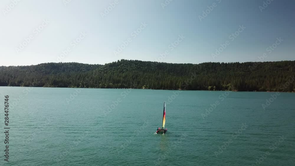 A sailboat with a rainbow sail drifts on Scott's Flat lake in the Sierra Nevada, California A sailboat with a rainbow sail drifts on Scott's Flat lake in the Sierra Nevada, California