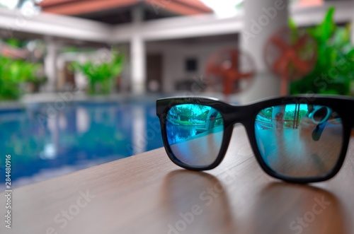 Blue sunglasses are placed on a poolside table. Summer holiday view. © SPINOKIM