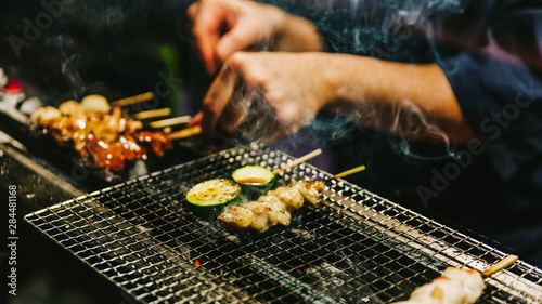 Close-up hands of Japanese Yakitori Chef grilling chicken marinated with ginger, garlic and soy sauce and cucumber with a lot of smoke. photo