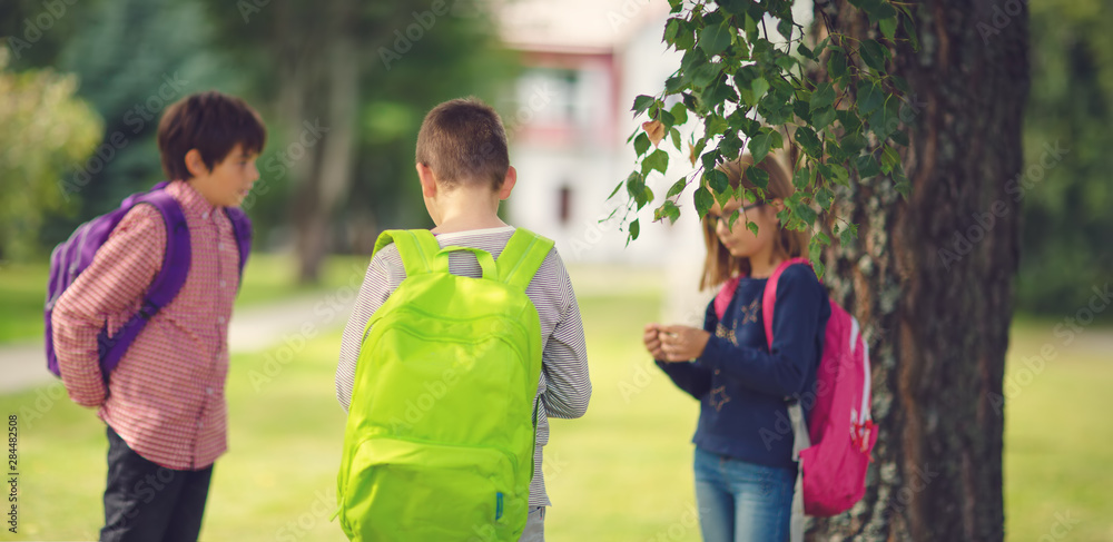 Obraz premium Children with rucksacks standing in the park near school