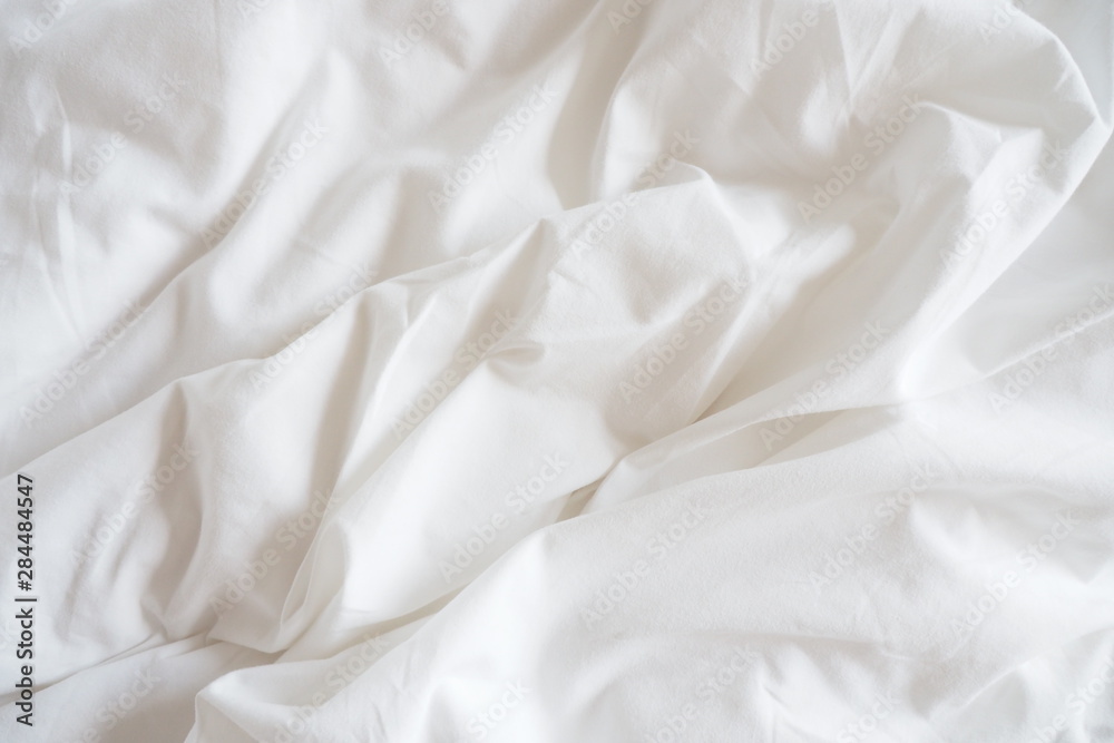 Closeup of beautiful white shiny crumpled polyester fabric sheets on the bed with warm motion and feeling for background and decoration. Cloth washing and laundry concept at home