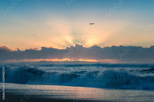 Epic sunrise seascape with sun beaming through the clouds and air plane