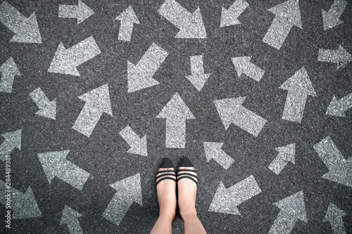 Feet and arrows on road background. Woman standing with many direction sign arrow choices in different ways, left and forward. Taking decisions for the future female. Top view of selfie foot and shoe.