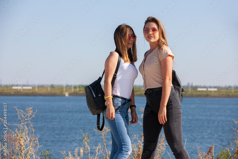 two beautiful young and stylish girl sitting in a summer city near water
